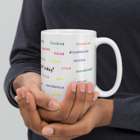 White mug with various feeling words written around the mug in rainbow colors.